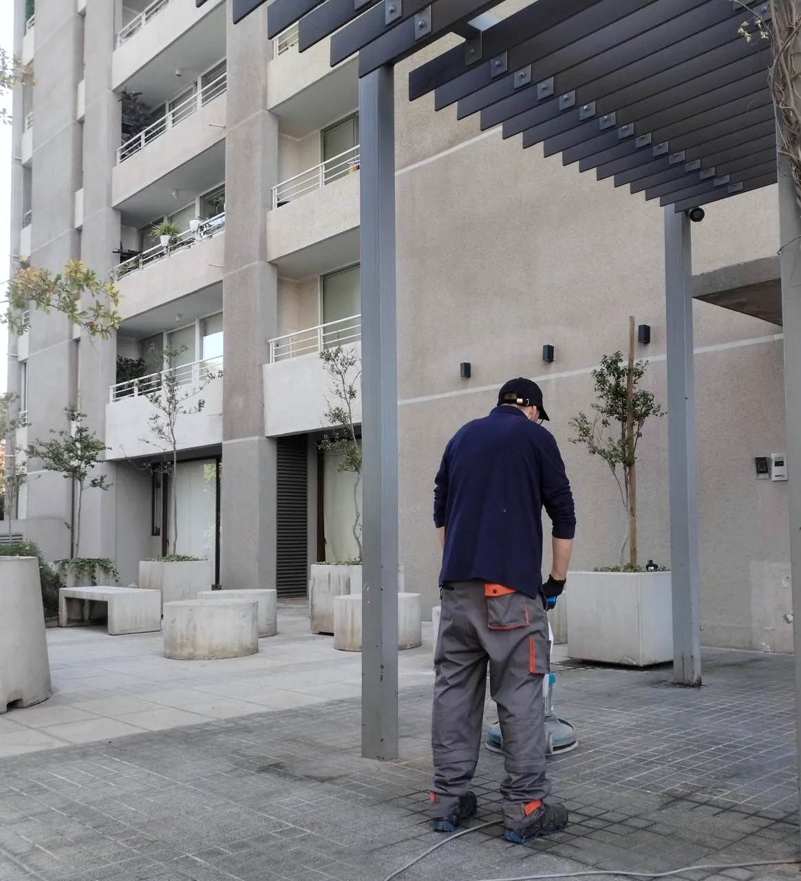 Colaborador de 3D Group con uniforme y EPP realizando mantención de pavimentos en el patio de un edificio